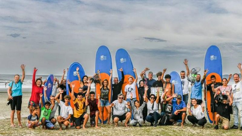 Alunos e professores de surf em modalidade gratuita oferecida pela prefeitura Grupo de surf Pessoas com as mãos para cima e prancha de surf atrás - Reprodução/Instagram