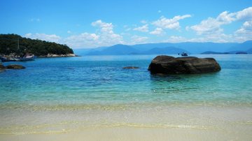 Praia Grande (Ubatuba) com céu azul, água do mar azul, prédios ao fundo e muitos banhistas pela faixa de areia - Guilherme Nigro