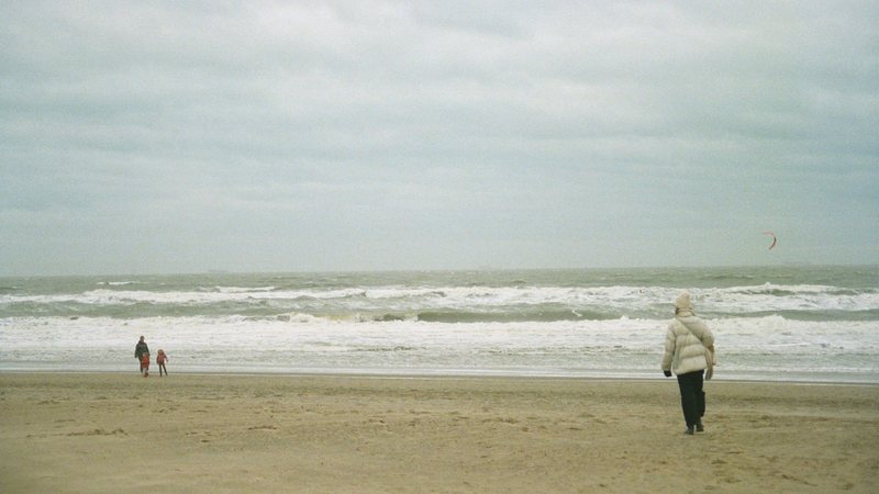 Pessoas agasalhadas caminham pela praia