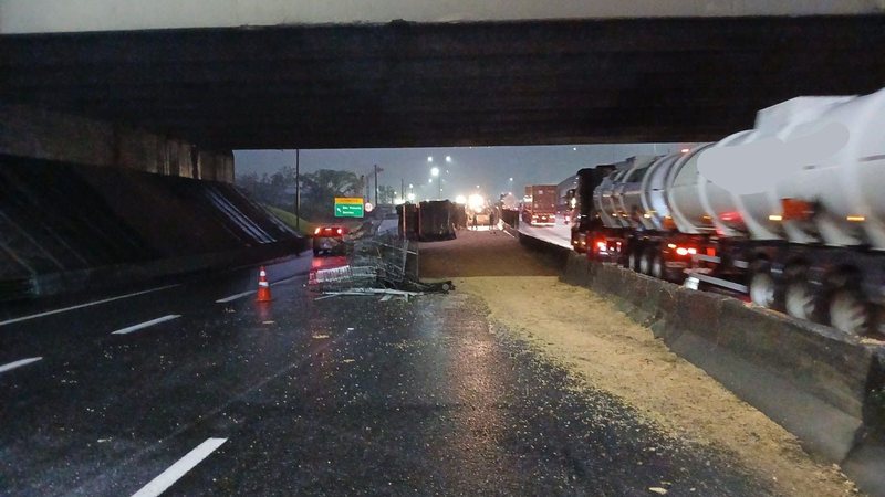 Caminhão tombado e carga de soja despejada na pista