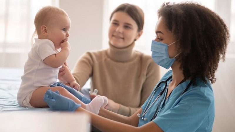 Bebê na sala de vacinação, com responsável e enfermeira