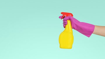 Mão com luva de borracha e spray de produto de limpeza