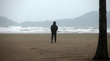Homem caminhado agasalhado na praia de Santos