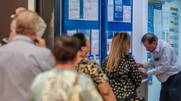 Pessoas aguardando na fila da lotérica para apostar e homem preenchendo cartela de aposta