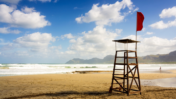 Praia com bandeira vermelha indicando imprópria para banho