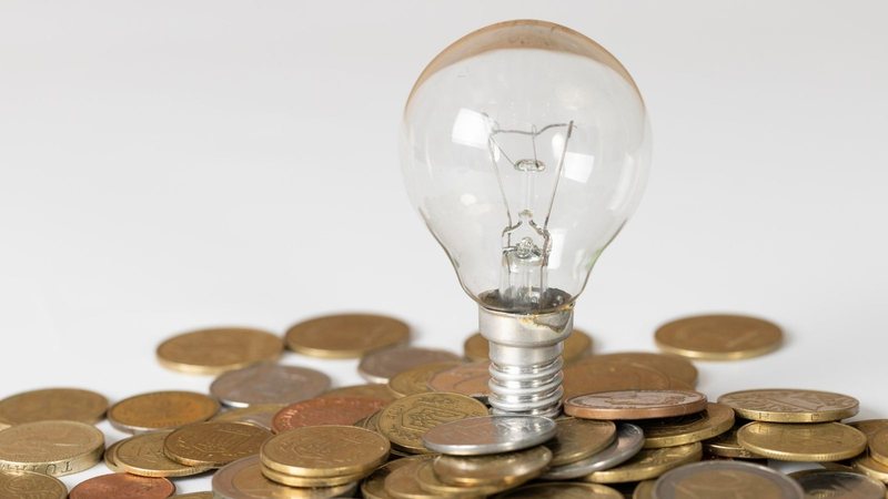 Lâmpada acesa cercada por moedas simbolizando economia de energia com desconto social na conta de luz