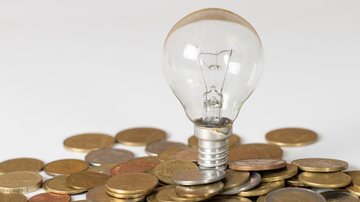 Lâmpada acesa cercada por moedas simbolizando economia de energia com desconto social na conta de luz
