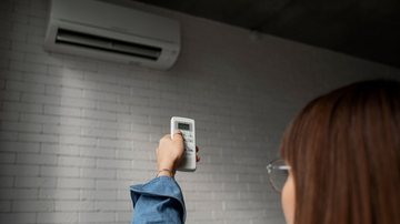 Mulher usando controle de ar-condicionado para manter a casa fresca
