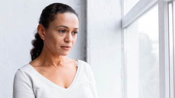 Mulher de meia-idade com expressão triste olhando para uma janela