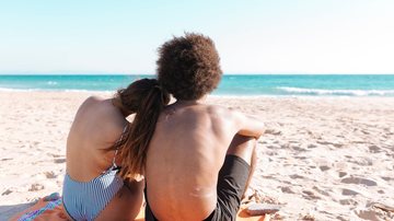 Casal de costas sentado lado a lado na areia da praia