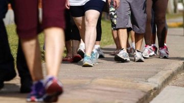 Pessoas caminham ao ar livre em ritmo constante, usando roupas esportivas, durante atividade física diária