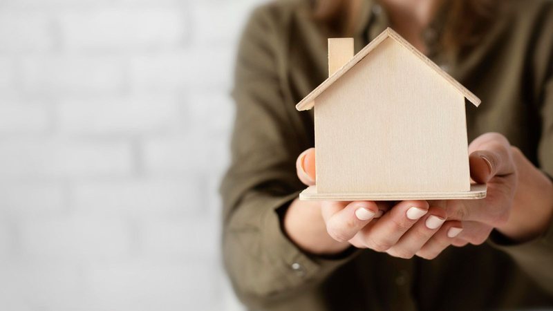 Pessoa segura a miniatura de uma casa nas mãos