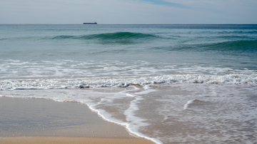 Orla de praia com maré alta e barco ao fundo
