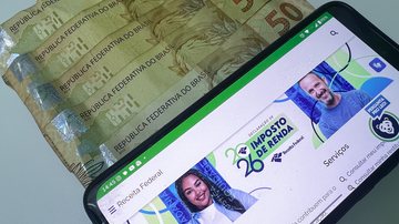 Notas de R$50 e celular com o site do Imposto de Renda na tela