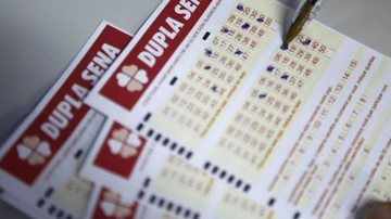 A imagem mostra o vários volantes da Dupla Sena, loteria da Caixa Econômica Federal, com uma caneta selecionando os números escolhidos para jogar no concurso.