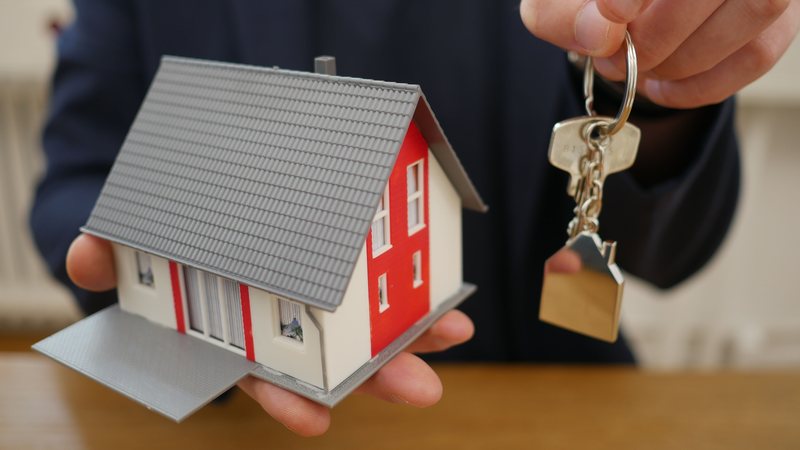 Homem segurando miniatura de uma casa na mão esquerda e chave na mão direita