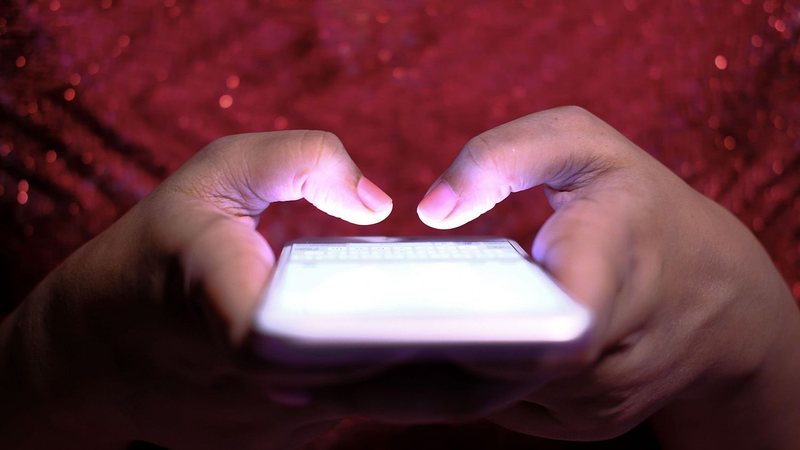 Pessoa segurando e utilizando um celular com a tela iluminada