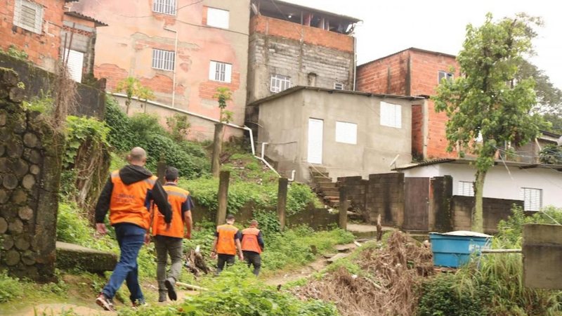Imagem de casas em morro de Santos, e agentes da Defesa Civil na parte de baixo da imagem