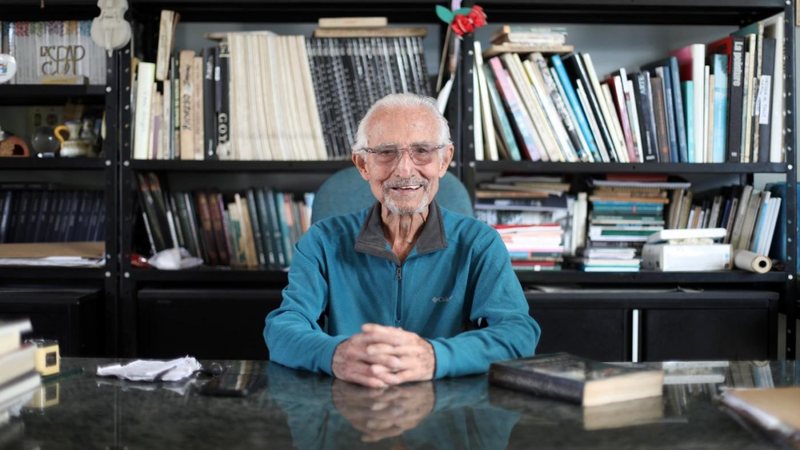Imagem do escultor Luis Garcia Jorge sentado atrás de um balcão, posando para a foto