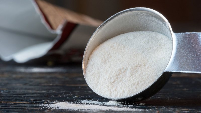 Goma xantana em pó em uma colher medidora, com parte do ingrediente espalhado
