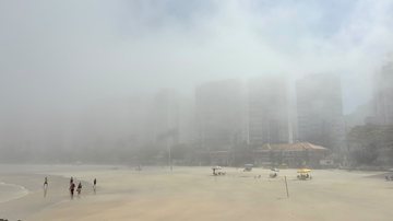 A imagem mostra uma orla marítima fortemente coberta por um denso nevoeiro marítimo, que reduz drasticamente a visibilidade e oculta a paisagem do mar dos prédios