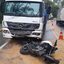 A imagem mostra um grave acidente de trânsito envolvendo uma motocicleta caída no asfalto e a parte frontal danificada de um caminhão branco da marca Mercedes-Benz (modelo Atego), com marca d'água de registro da ARTESP na pista