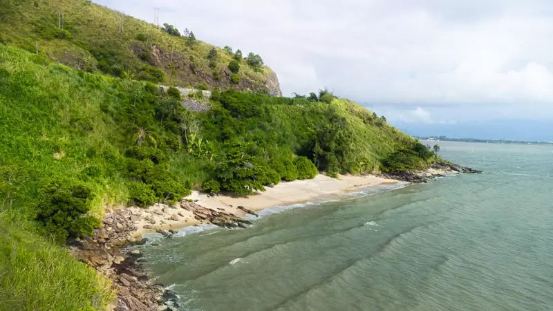 Vista aérea da Praia da Tatuíra, em São Sebastião, com pequena faixa de areia cercada por vegetação preservada, encostas e mar de águas calmas