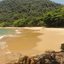Faixa de areia clara, mar de águas tranquilas e vegetação de Mata Atlântica