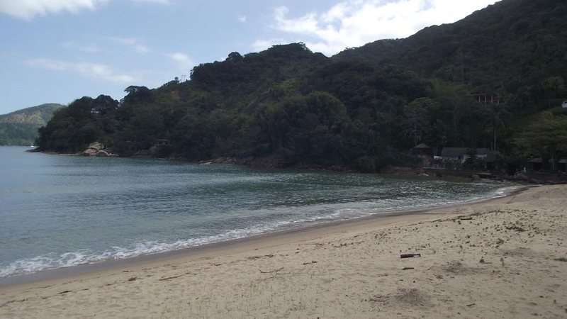Praia do Perequê-Mirim, com faixa de areia, mar calmo e morros cobertos por vegetação ao redor