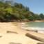 Faixa de areia clara, pedras espalhadas, mar calmo de águas azul-esverdeadas e Mata Atlântica