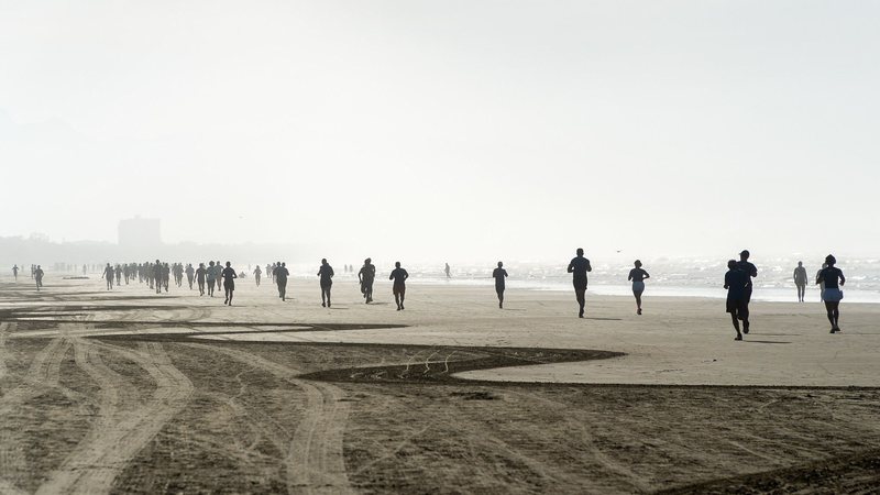 Pessoas correndo na faixa de areia da praia da Enseada, no início da manhã