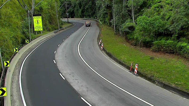 Trecho da rodovia, em meio à vegetação, com carro trafegando e sinalização indicando obras na pista
