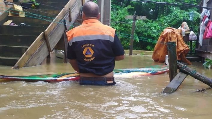 Imagem de agente da Defesa Civil de Ubatuba, de costas, em meio a enchente