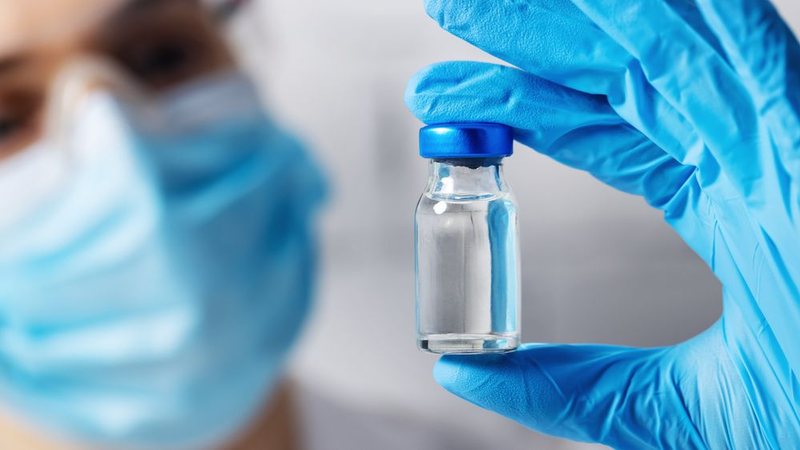 Profissional de saúde usando luvas azuis segura um frasco de vacina
