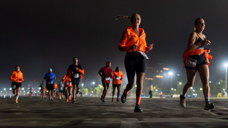 Imagem de diversos atletas correndo na praia a noite