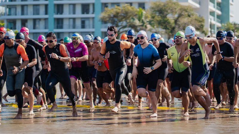 Imagem de diversos atletas com roupas de banho correndo para entrar na água do mar
