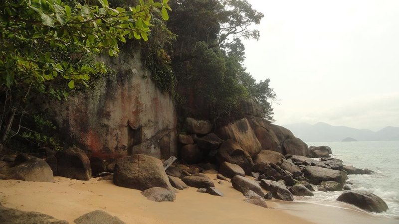 Praia do Meio com faixa de areia cercada por grandes pedras e vegetação