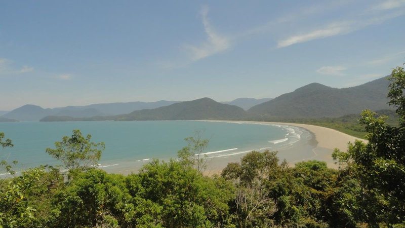 Praia da Fazenda, com extensa faixa de areia, mar tranquilo, vegetação e montanhas