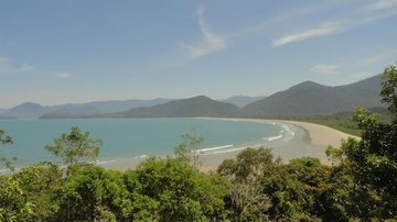 Praia da Fazenda, com extensa faixa de areia, mar tranquilo, vegetação e montanhas
