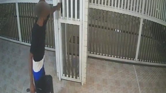 Imagem mostra uma gravação de câmera de segurança que registra a ação de um homem próximo ao portão de um condomínio