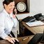 Agente de recepção enquanto fala ao telefone e utiliza um computador