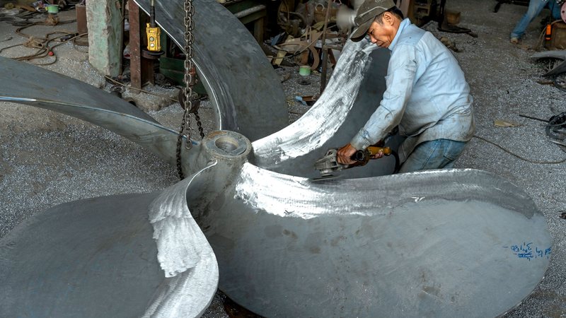 Montador naval trabalha no acabamento de uma grande hélice metálica