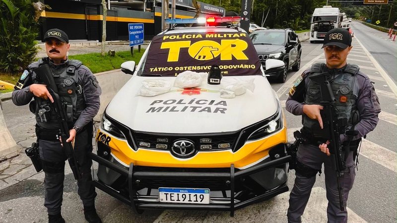 Imagem mostra agentes da PM Rodoviária ao lado da viatura da corporação