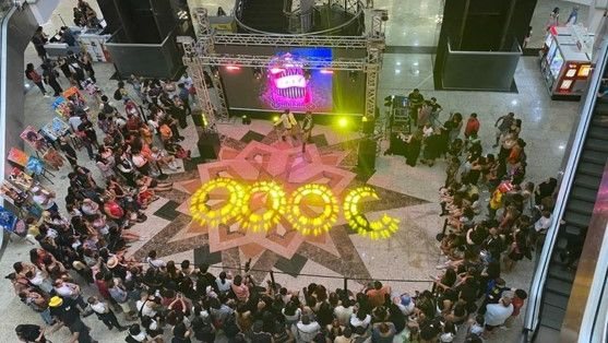 Praça central do shopping com um telão e pessoas reunidas