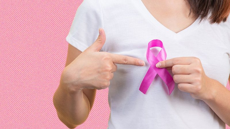 Mulher aponta para um laço rosa símbolo da campanha de conscientização e prevenção do câncer de mama