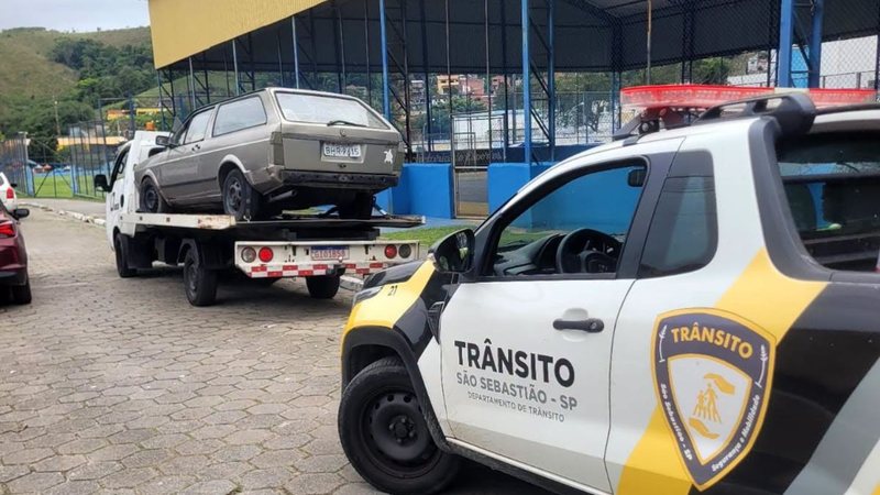 Imagem mostra uma viatura do Departamento de Trânsito de São Sebastião acompanhando a remoção de um veículo antigo (uma Volkswagen Brasília) em uma via pública da cidade