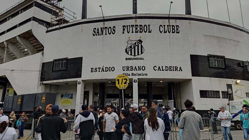 Imagem da frente da Vila Belmiro com torcedores do Santos nos arredores