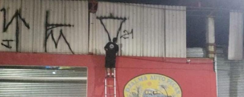 Imagem Imagem flagra homem pendurado em escada pichando fachada de loja em Ubatuba