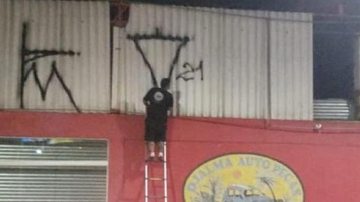 Imagem Imagem flagra homem pendurado em escada pichando fachada de loja em Ubatuba