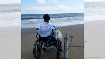 Alex da Conceição Araújo mora a 280 km da capital do Maranhã e realizou o desejo de ir à praia, mesmo internado Equipe médica cria experiência inédita e leva UTI para a praia Jovem de costas sentado em cadeira de rodas com equipamentos de UTI admirando o c - Reprodução/Instagram